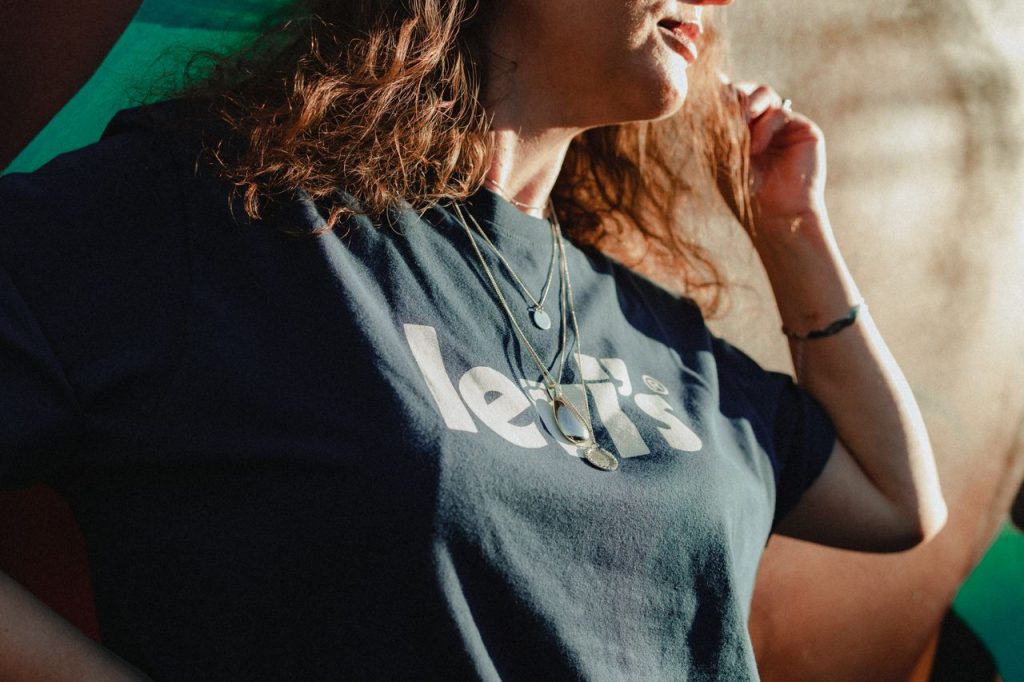 Stylish woman in a black graphic tee and necklaces, outdoors in natural light.