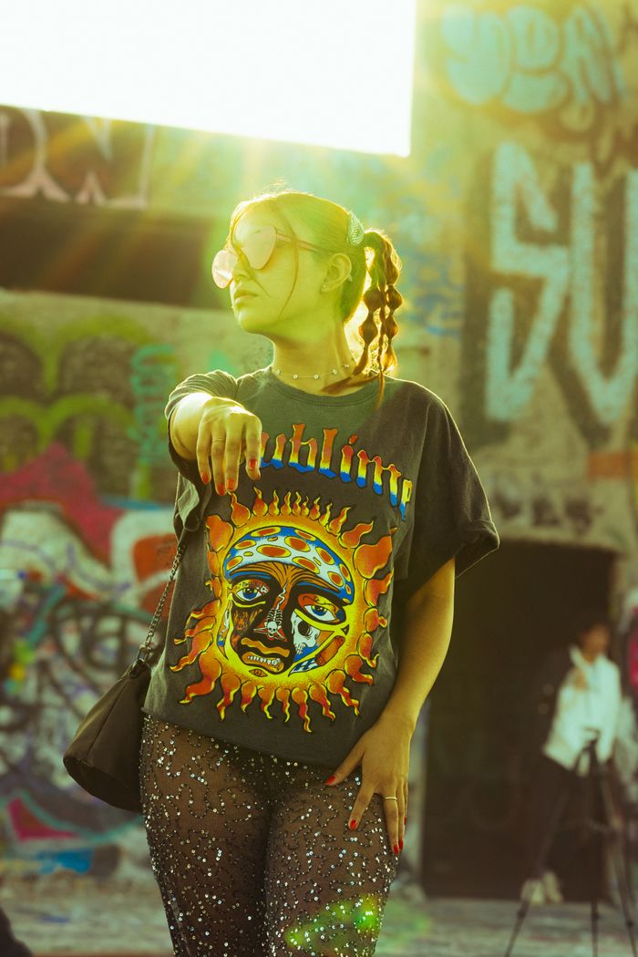 Stylish woman in graphic tee posing in front of vibrant graffiti under golden sunlight.
