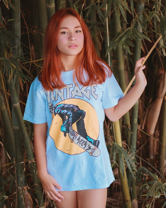 Stylish woman with red hair posing outdoors against bamboo wearing a graphic tee.